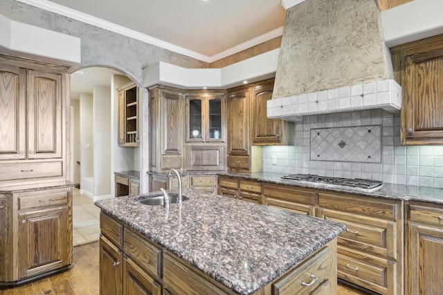 kitchen with stainless steel gas cooktop, crown molding, a kitchen island with sink, and hardwood / wood-style flooring