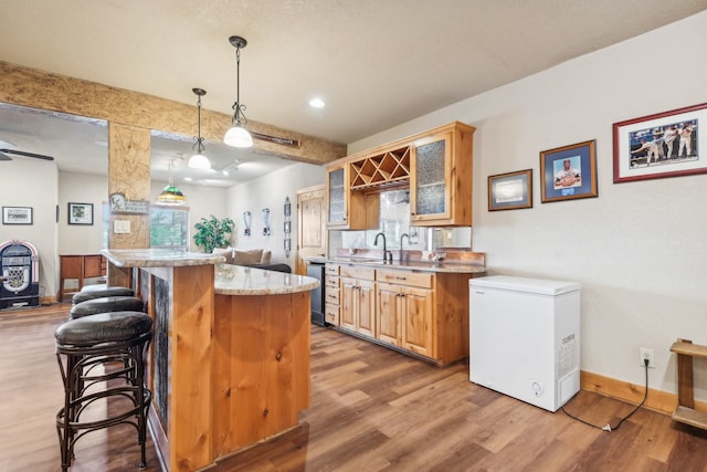 kitchen with a kitchen island, a kitchen breakfast bar, light hardwood / wood-style flooring, fridge, and pendant lighting