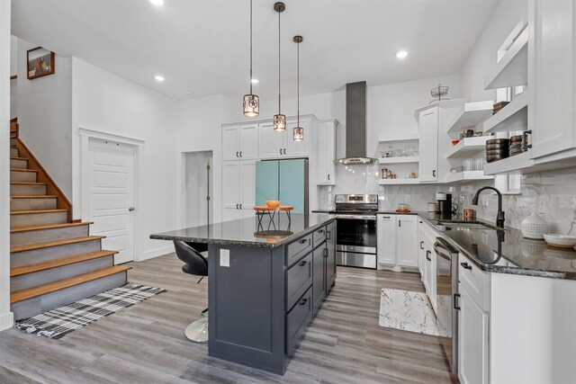 kitchen featuring wall chimney range hood, sink, a center island, white cabinetry, and stainless steel appliances