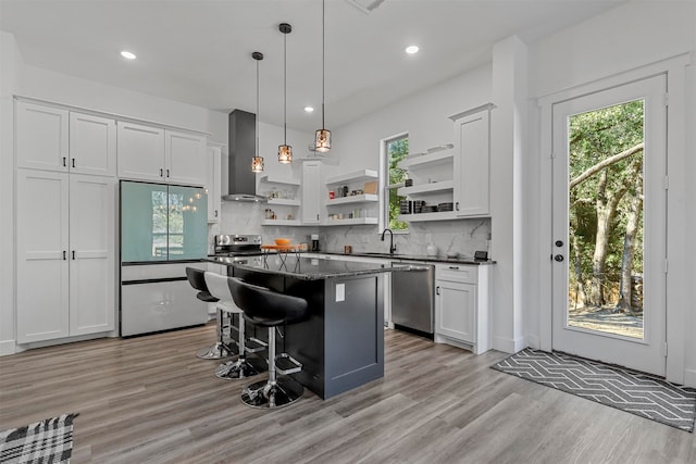 kitchen with a kitchen island, wall chimney exhaust hood, a kitchen breakfast bar, stainless steel appliances, and light hardwood / wood-style floors