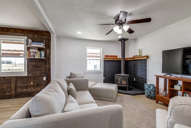 living room featuring light wood-type flooring, a wood stove, ceiling fan, and ornamental molding