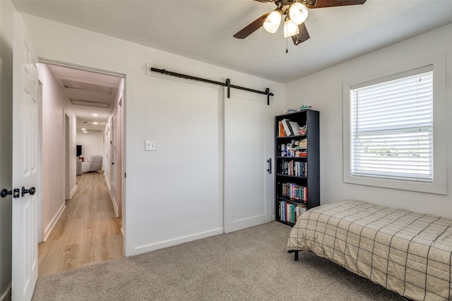 carpeted bedroom with ceiling fan and a barn door