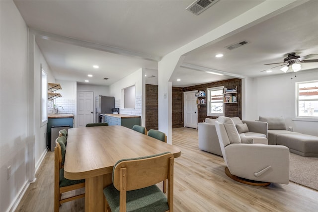 dining space with brick wall, light wood-type flooring, ceiling fan, and sink