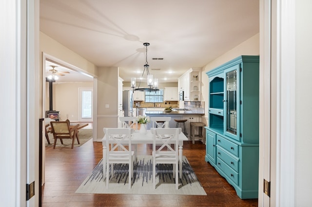 dining space featuring a wood stove, dark hardwood / wood-style flooring, and ceiling fan with notable chandelier