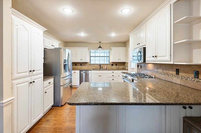 kitchen with white cabinets, kitchen peninsula, stainless steel appliances, and dark stone countertops