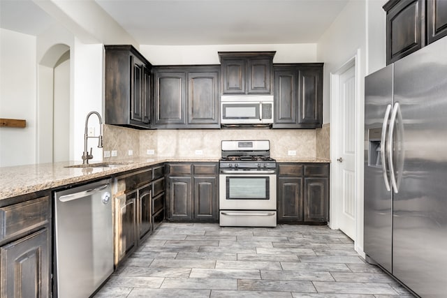 kitchen featuring sink, appliances with stainless steel finishes, light stone countertops, light hardwood / wood-style flooring, and decorative backsplash