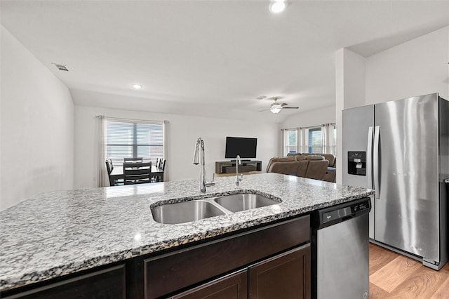 kitchen with stainless steel appliances, sink, light stone counters, ceiling fan, and light hardwood / wood-style floors