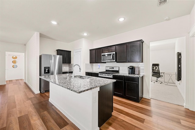 kitchen featuring stainless steel appliances, sink, light stone counters, tasteful backsplash, and an island with sink