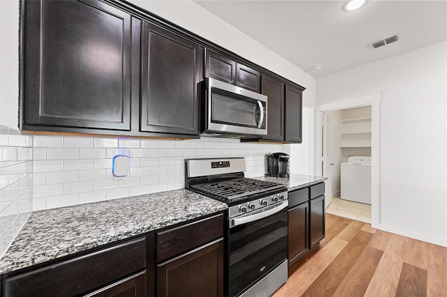 kitchen featuring stainless steel appliances, light wood-type flooring, dark stone counters, washer / dryer, and dark brown cabinets