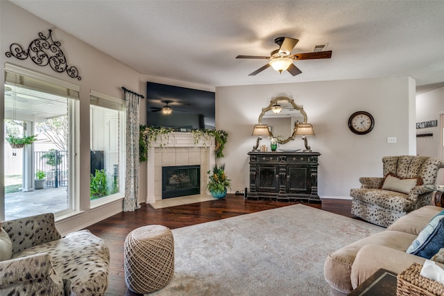 living room featuring a textured ceiling, dark wood-type flooring, a tile fireplace, and ceiling fan