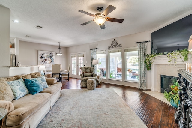 living room featuring french doors, a fireplace, hardwood / wood-style flooring, a textured ceiling, and ceiling fan