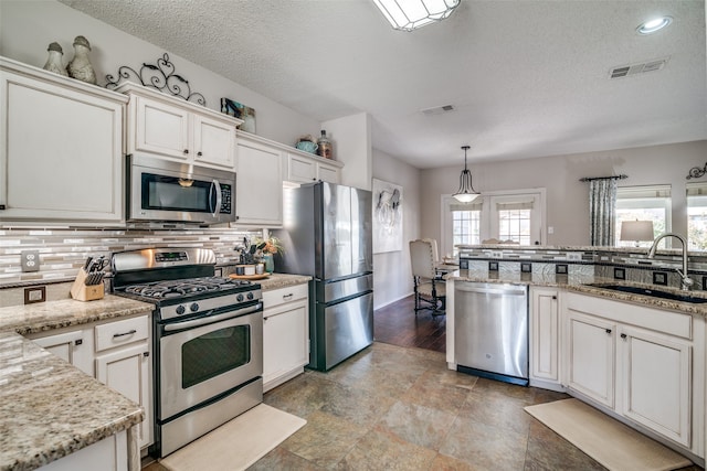 kitchen with hanging light fixtures, stainless steel appliances, sink, white cabinetry, and a textured ceiling