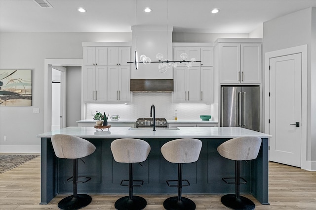 kitchen with light hardwood / wood-style floors, an island with sink, white cabinets, and high end appliances