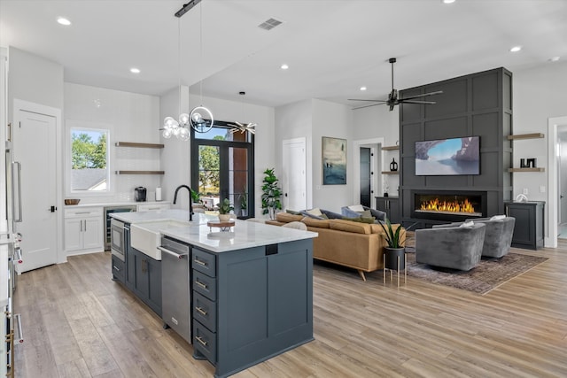 kitchen featuring sink, a fireplace, white cabinets, light hardwood / wood-style flooring, and a center island with sink