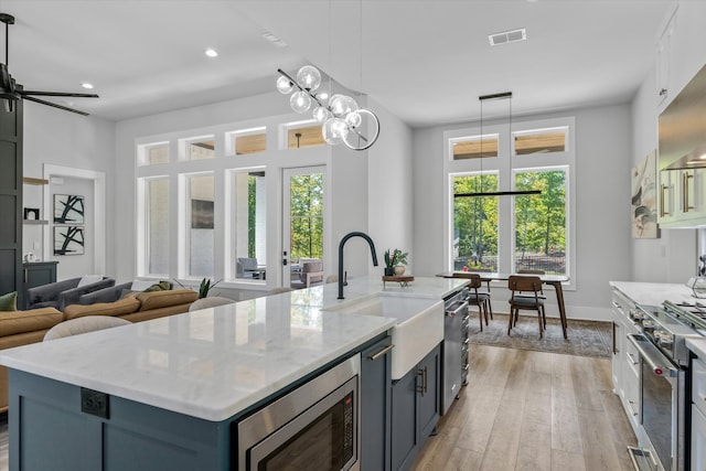 kitchen featuring a center island with sink, sink, pendant lighting, light hardwood / wood-style floors, and stainless steel appliances