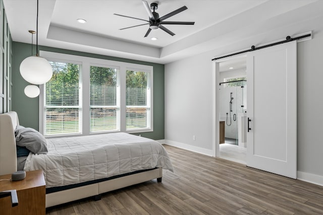 bedroom featuring ceiling fan, a tray ceiling, a barn door, and hardwood / wood-style floors