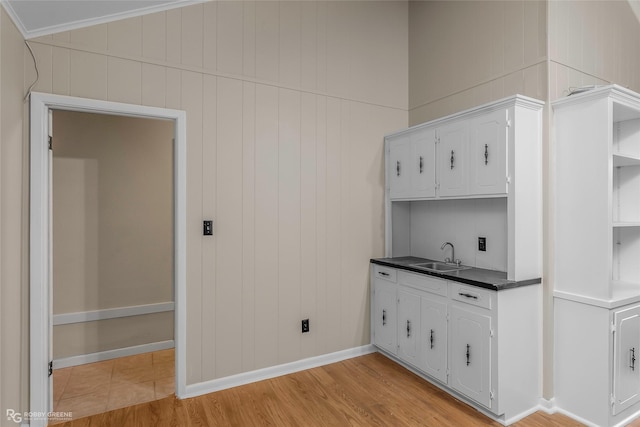 kitchen featuring baseboards, light wood finished floors, a sink, white cabinets, and dark countertops