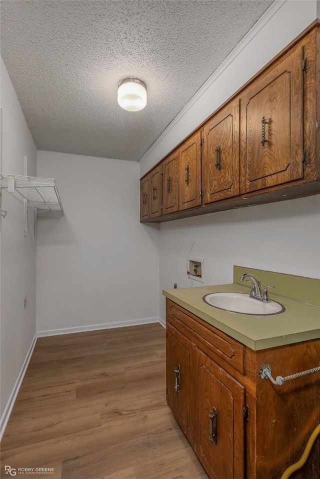 clothes washing area featuring light wood finished floors, hookup for a washing machine, cabinet space, a textured ceiling, and a sink