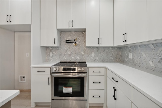 kitchen with light stone countertops, white cabinetry, tasteful backsplash, and electric range