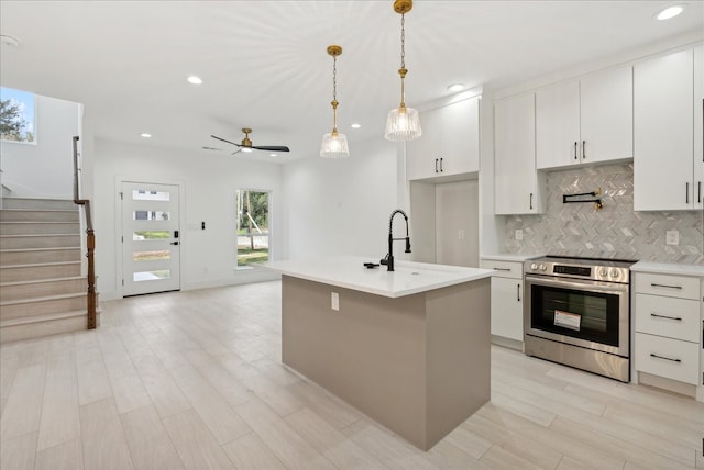 kitchen with an island with sink, decorative light fixtures, white cabinets, light hardwood / wood-style floors, and electric stove