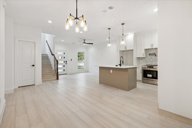 kitchen with a kitchen island with sink, pendant lighting, light wood-type flooring, stainless steel range with electric cooktop, and white cabinetry