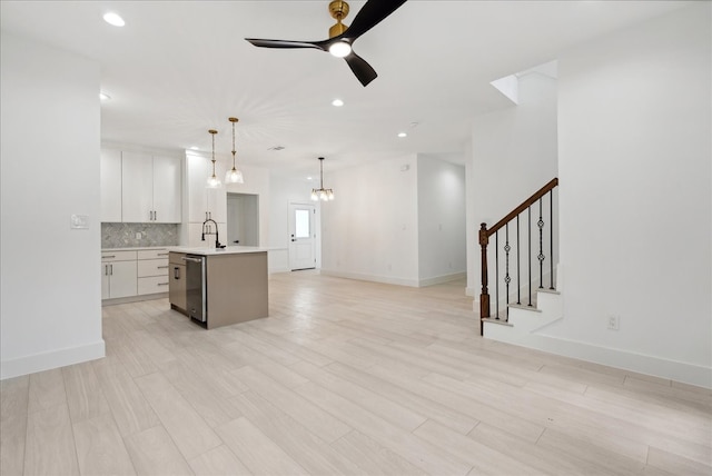 kitchen featuring white cabinets, an island with sink, ceiling fan with notable chandelier, light hardwood / wood-style floors, and decorative light fixtures