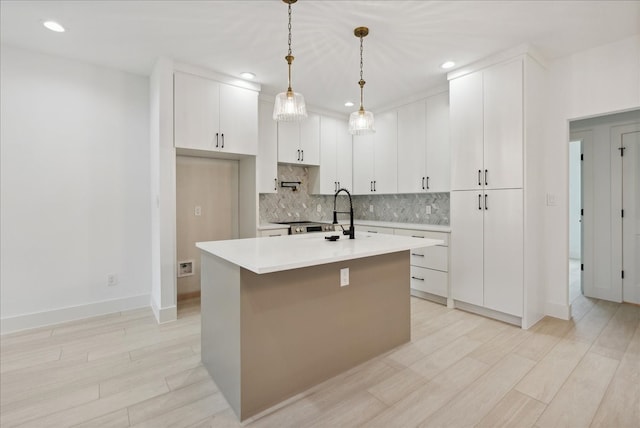 kitchen with an island with sink, backsplash, pendant lighting, light wood-type flooring, and white cabinetry