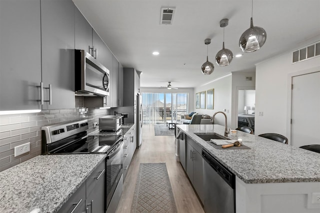 kitchen with sink, light wood-type flooring, an island with sink, hanging light fixtures, and stainless steel appliances