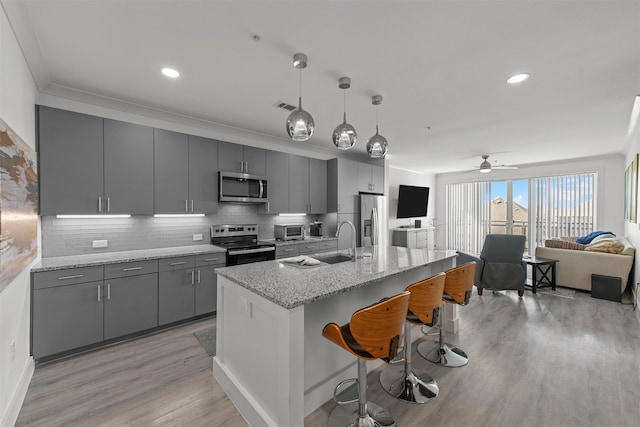 kitchen featuring gray cabinetry, light stone countertops, appliances with stainless steel finishes, and a breakfast bar