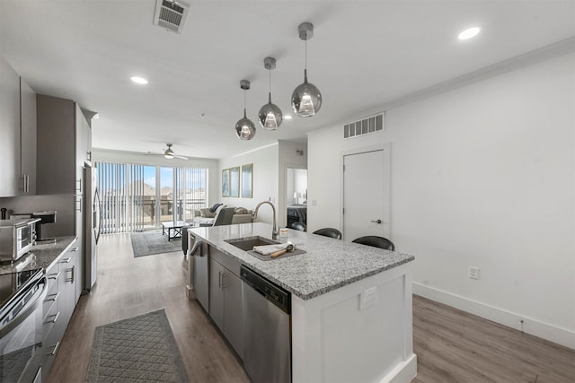 kitchen with hanging light fixtures, a center island with sink, sink, hardwood / wood-style floors, and appliances with stainless steel finishes