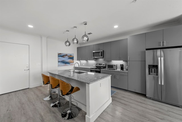 kitchen with gray cabinetry, stainless steel appliances, sink, and a kitchen island with sink