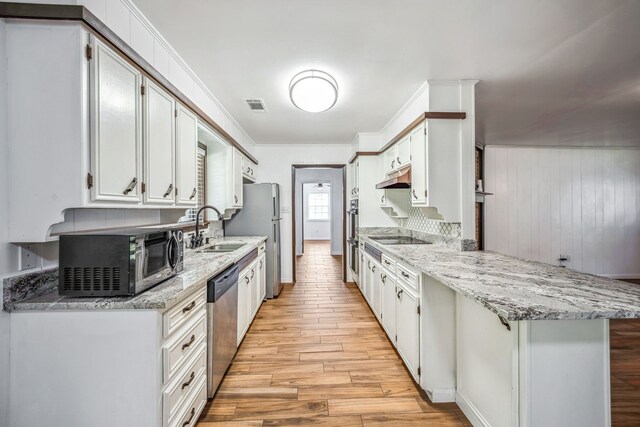 kitchen with kitchen peninsula, sink, white cabinets, light wood-type flooring, and appliances with stainless steel finishes