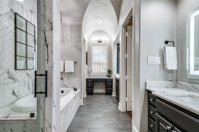 bathroom featuring vanity, lofted ceiling, and tiled tub