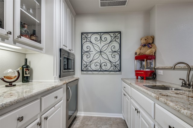 kitchen with light stone countertops, sink, washer / dryer, white cabinetry, and stainless steel microwave