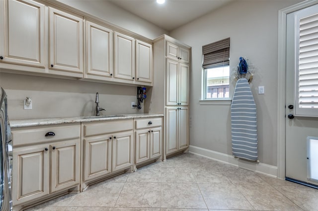 laundry area featuring sink, light tile patterned floors, and cabinets