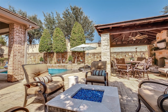 view of patio / terrace featuring ceiling fan, an outdoor fire pit, an outdoor stone fireplace, pool water feature, and a fenced in pool