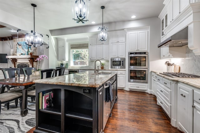 kitchen with sink, light stone counters, a center island with sink, white cabinets, and appliances with stainless steel finishes