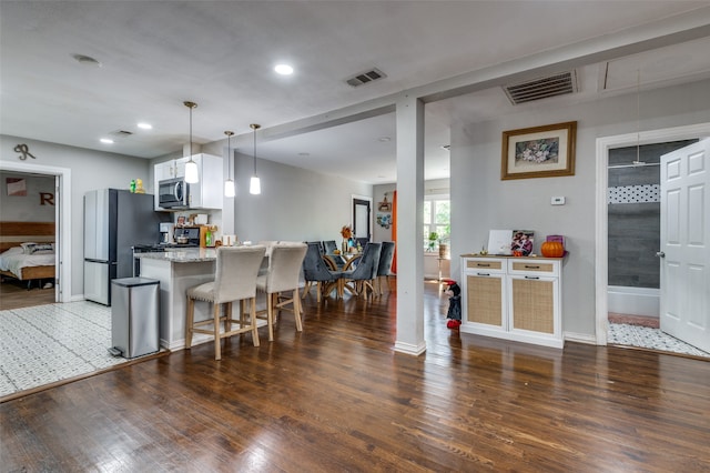 kitchen with kitchen peninsula, a breakfast bar area, appliances with stainless steel finishes, light stone countertops, and dark wood-type flooring