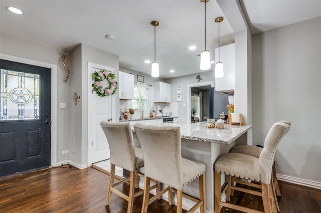 kitchen featuring a breakfast bar area, white cabinetry, dark hardwood / wood-style floors, pendant lighting, and light stone counters