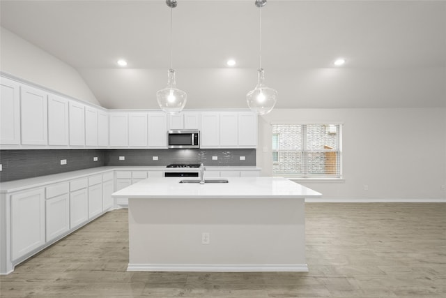 kitchen featuring lofted ceiling, sink, white cabinetry, a center island with sink, and decorative light fixtures