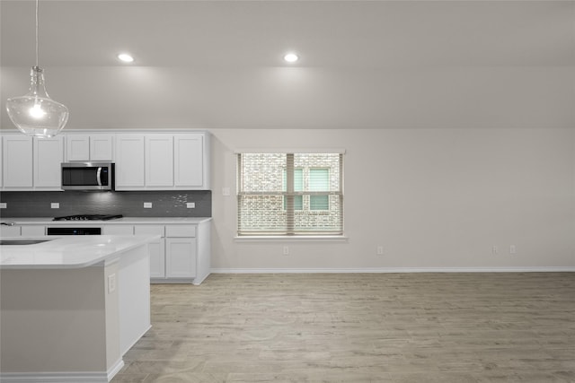 kitchen featuring light stone counters, hanging light fixtures, light wood-type flooring, decorative backsplash, and white cabinets