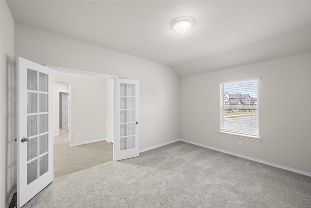 unfurnished room with vaulted ceiling, light colored carpet, and french doors