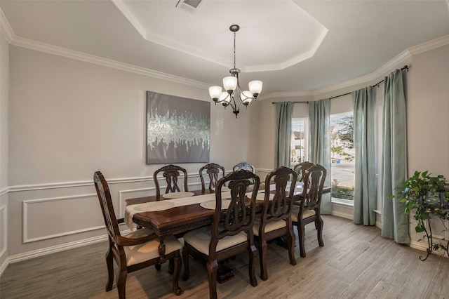 dining space with ornamental molding, hardwood / wood-style floors, a tray ceiling, and an inviting chandelier