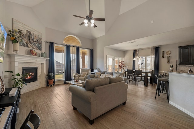 living room featuring high vaulted ceiling, ceiling fan with notable chandelier, hardwood / wood-style flooring, and a healthy amount of sunlight