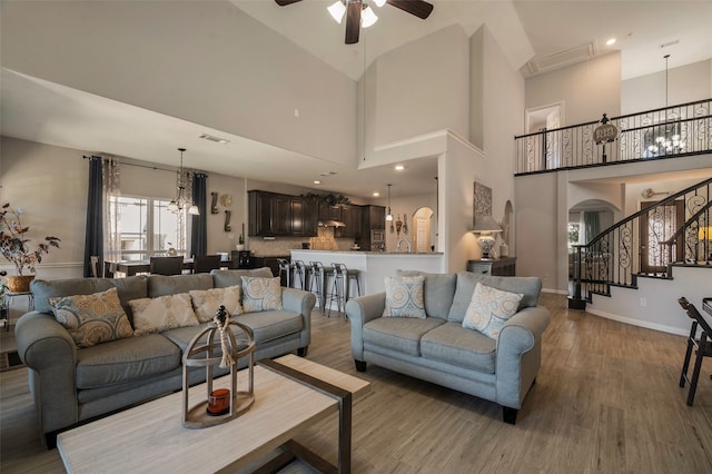 living room featuring hardwood / wood-style flooring, ceiling fan with notable chandelier, and a high ceiling