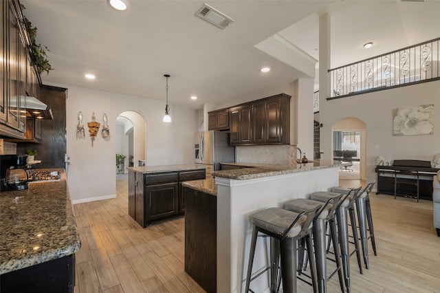 kitchen featuring stainless steel fridge with ice dispenser, backsplash, a kitchen island, light hardwood / wood-style flooring, and dark stone countertops