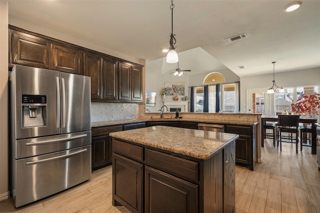 kitchen with hanging light fixtures, kitchen peninsula, stainless steel appliances, a center island, and light hardwood / wood-style floors