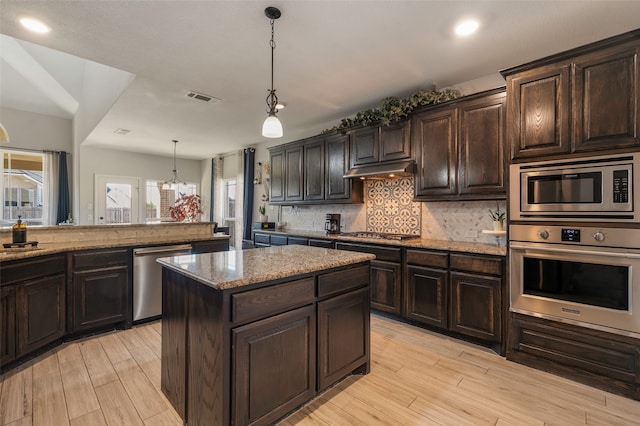 kitchen featuring appliances with stainless steel finishes, decorative light fixtures, dark brown cabinets, and a kitchen island