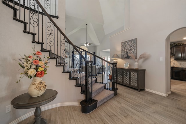 staircase featuring hardwood / wood-style flooring, high vaulted ceiling, and ceiling fan