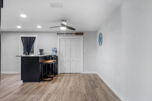 kitchen featuring ceiling fan, light stone countertops, a breakfast bar, and light wood-type flooring